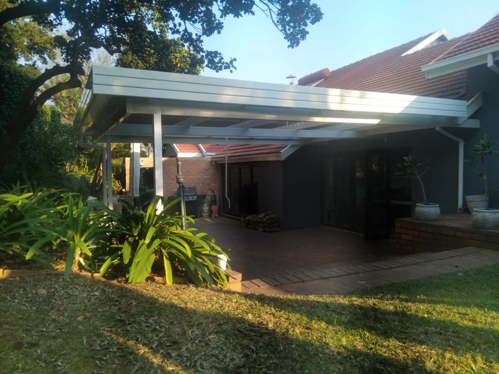 White aluminium louvre awning cantilevered over a brick-paved patio at a tile-roof home